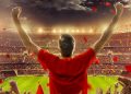 A football fan in red celebrating in a packed stadium as confetti falls